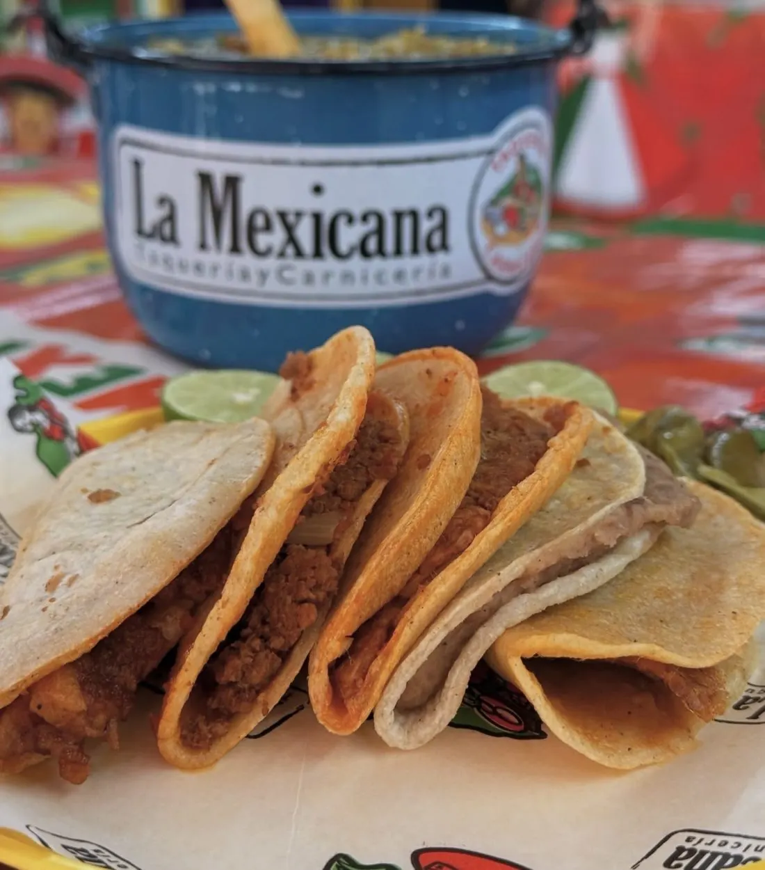 Tacos de canasta de La Mexicana con la cubeta de salsa de la casa sobre papel de la marca